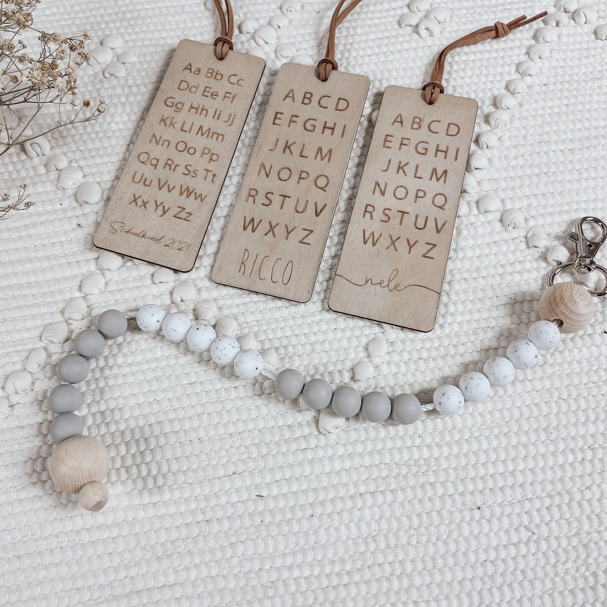 Drei aufgereihte Lesezeichen aus Holz mit Lederband und Schnullerkette im Vordergrund