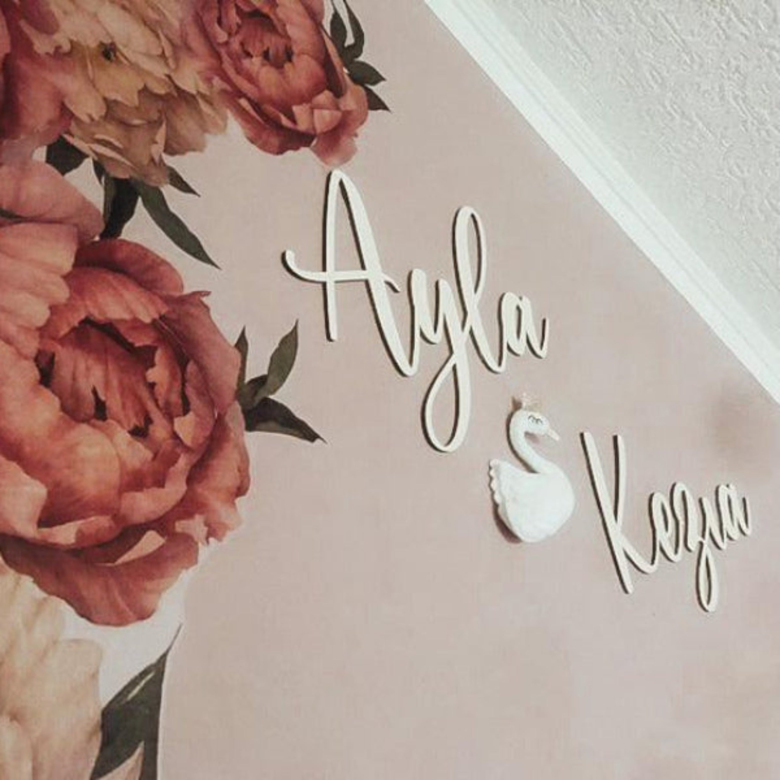 Zwei aus Holz gelaserter Kindernamen mit Schwannmotiv auf rose Wand mit Blumenmuster